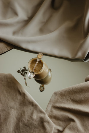 Coffee with milk and a original spoon in a glass tumbler in the middle of a mirror on an isolated beige background.の写真素材