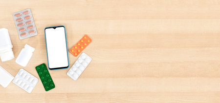 Smart phone with blank screen and pills, on wooden desktop. Top view.の写真素材