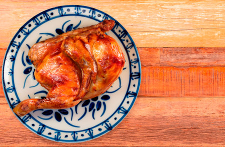 Close up of half roasted chicken on plate over rustic wooden background.