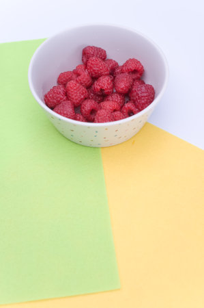 sweet tasty raspberries in a bowl on multicolored background and copy spaceの写真素材