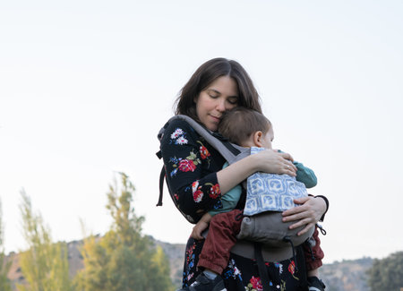 Young mother with her toddler kid boy on back in ergonomic baby carrier in autumn nature. Active mother conceptの写真素材