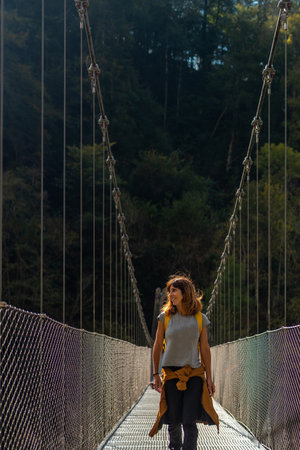 A hiker with a yellow backpack crossing the Holtzarte suspension bridge, Larrau. In the forest or...