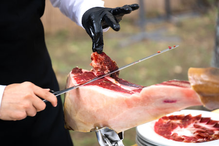 The chef is cutting the ham. image of a ham cutter with a knife cutting a thin slice of ham. Dried Ham, Serrano Ham, Acorn, Iberian, Italian or Parma Raw Prosciuttoの写真素材