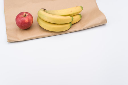 ripe biologic red apple and bananas on a white and  background and paper bag with copy spaceの写真素材