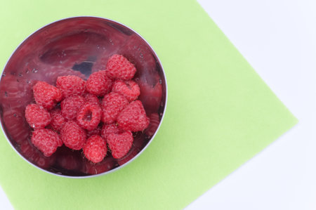 sweet tasty raspberries in a bowl on multicolored background and copy space