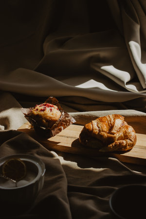Close-up image of a croissant and a muffin on a wooden board with a beige background in strong light.の写真素材