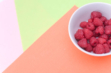 sweet tasty raspberries in a bowl on multicolored background and copy spaceの写真素材