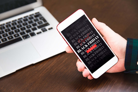 Hand holding cellphone with black friday text. Concept of sales, online shopping, and e-commerce.