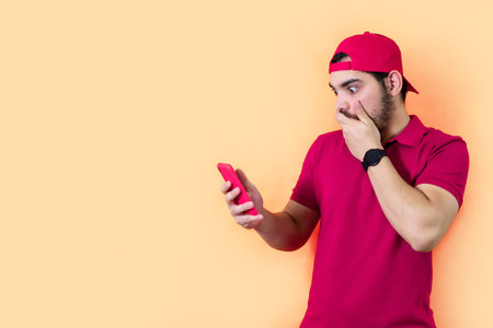 Young man surprised while checking his cell phone, on yellow background.の写真素材