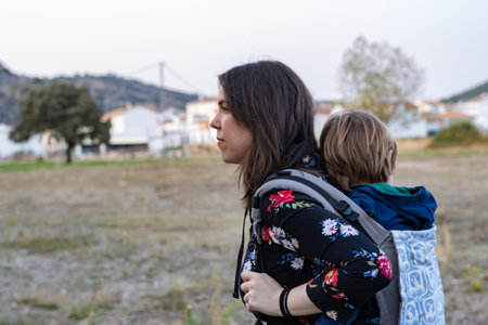 Young mother with her toddler kid boy on back in ergonomic baby carrier in autumn nature. Active...