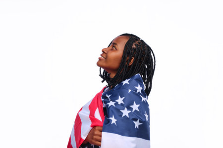 Side view of a young African American woman wrapped in USA flag looking up with against a white background.の写真素材