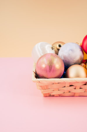 Multicolored Christmas decorative balls in a wicker canister with sapce for text on pink surfaceの写真素材