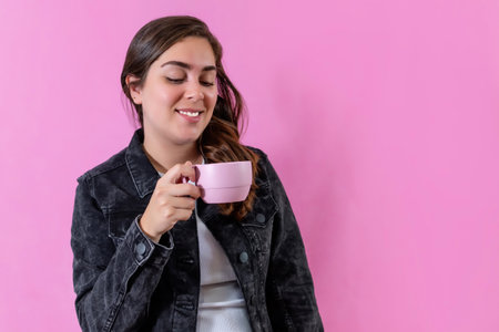 Casual woman drinking hot coffee on pink background.