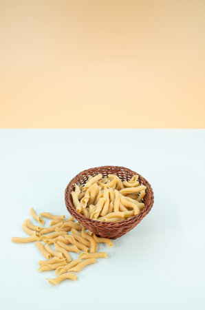 shot of italian torchiette pasta in a wicker canister on a pastel blue color backgroundの写真素材