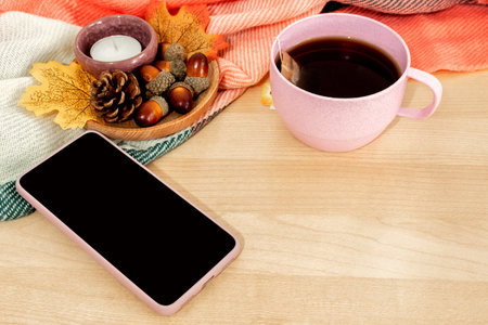 Tea cup, smart phone , candlelight, autumn leaves on wooden background.の写真素材