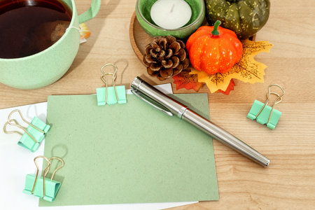 Autumn or winter season cozy composition with greeting card, tea cup, pen, on desk table.
