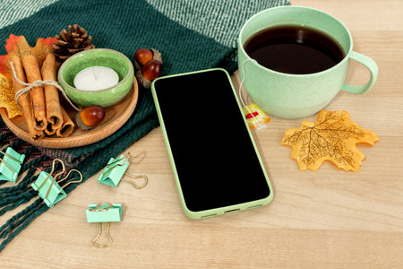 Winter still life. Tea cup with leaves and mobile phone on wooden background.の写真素材