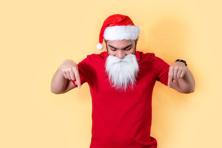 Santa Claus stands on yellow background, looks and shows thumbs down on copy space. Christmas and New Year.の写真素材