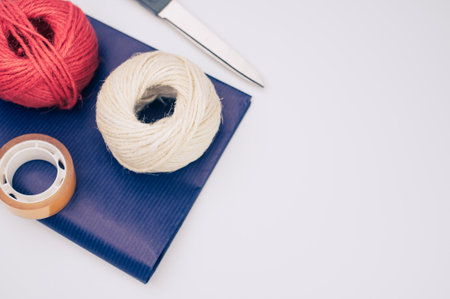 decorative yarn balls with blue paper sheet scissors and tape on a white surface