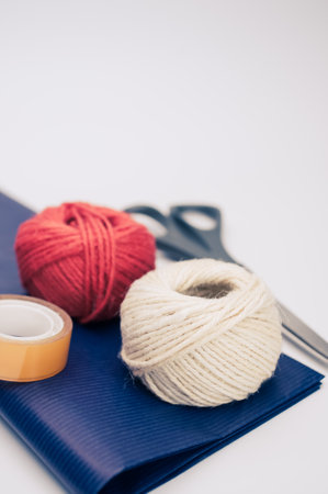 decorative yarn balls with blue paper sheet scissors and tape on a white surfaceの写真素材