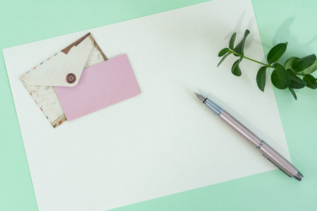 Top view of envelope and blank greeting card with pen on green background.