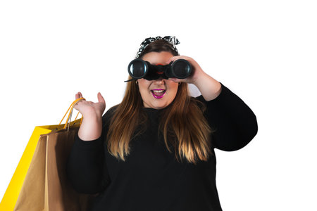 portrait of a plus size woman looking straight ahead with shopping bags and binoculars isolated on white background. Black friday concept, shopping, discountsの写真素材