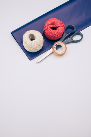 decorative yarn balls with blue paper sheet scissors and tape on a white surfaceの写真素材