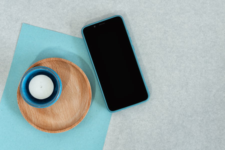 Blank smart phone, blue paper with candle and wooden dish, on gray background.の写真素材