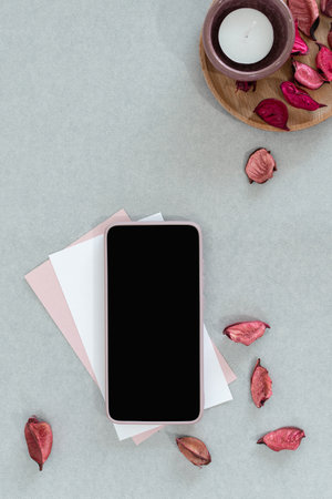 Blank smart phone, pink and white card with candle and petals, on gray background.の写真素材