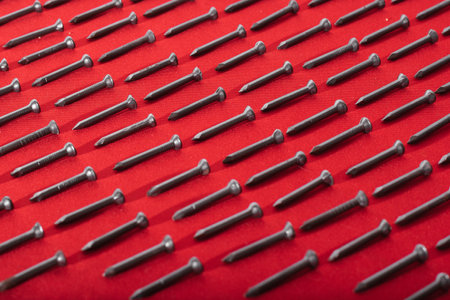 lot of black steel nails, on red background, arranged diagonally perfectly, concept of perfectionism and equalityの写真素材