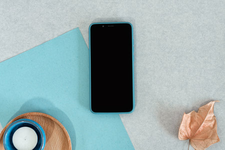 Blank smart phone, blue paper with candle and wooden dish, on gray background.