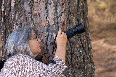 older white-haired woman taking pictures in the forestの写真素材
