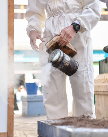 Close-up of beekeeper's hands with bee smoker smoking bees.