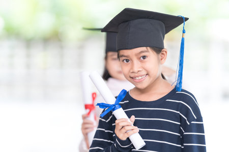 Happy Asian female school kid graduates with a graduation cap hold a rolled certificate celebrate graduation. Graduation Celebration Concept Stock Photoの写真素材