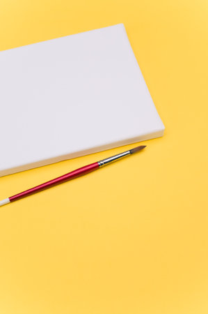 top view shot of blank white paint canvas and tools on a yellow paper surface with copy spaceの写真素材