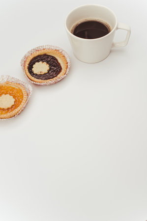 isolated apricot and cherry jam tart in a paper backing cup and cup of coffee on a white background with text spaceの写真素材