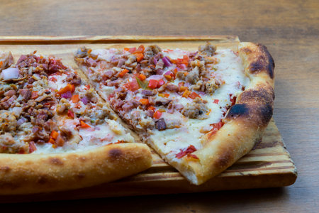 close-up of two triangles of pizza with cheese, chicken, bacon and vegetables on wooden board