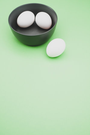 organic white eggs in a dark gray bowl on a  green surface with copy space for textの写真素材