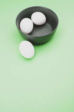 organic white eggs in a dark gray bowl on a  green surface with copy space for textの写真素材
