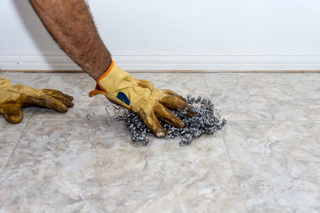 gloved hands of a person with no visible face removing dirt from a floor with steel shavingsの写真素材