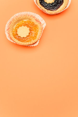 isolated apricot and cherry jam tart in a paper backing cup on orange background with text spaceの写真素材
