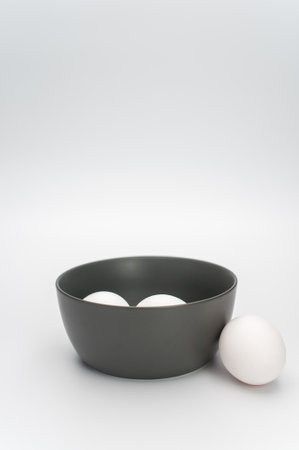 organic white eggs in a dark gray bowl on a white surface with copy space for textの写真素材