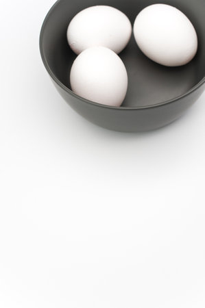 organic white eggs in a dark gray bowl on a white surface with copy space for text