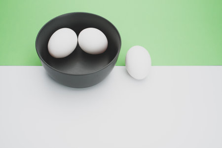 organic white eggs in a dark gray bowl on a white green surface with copy space for textの写真素材
