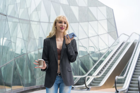 Entrepreneur girl business park in a modern building with escalator, young blonde in a suit sending...