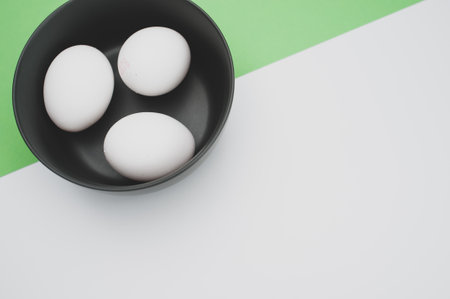 organic white eggs in a dark gray bowl on a white green surface with copy space for textの写真素材