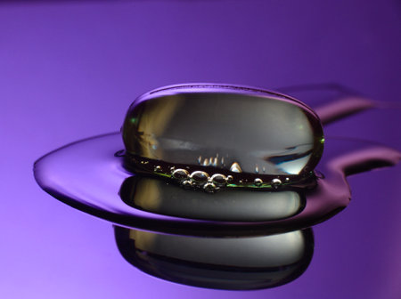 macro photography of a transparent medicinal capsule on reflective liquid. Violet colorsの写真素材