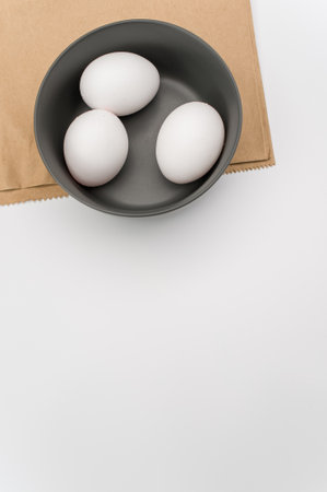 organic white eggs in a dark gray bowl on a food paper and white surface with copy space for textの写真素材
