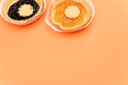 isolated apricot and cherry jam tart in a paper backing cup on orange background with text spaceの写真素材