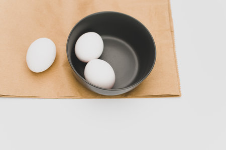 organic white eggs in a dark gray bowl on a food paper and white surface with copy space for text